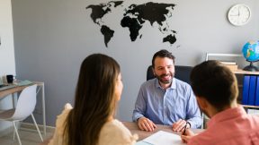 Deux étudiants sont assis dans un bureau avec un employé de l'université pour un entretien de conseil, avec une carte du monde au mur en arrière-plan.