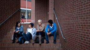 Studenten sitzen auf der Treppe eines roten Backsteingebäudes.
