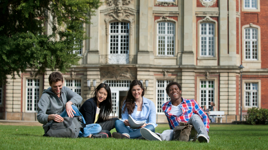 Four students sitting in front of a building on the lawn