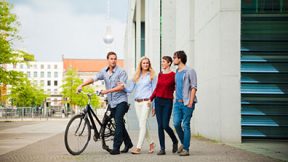 Quatre étudiants se promènent à vélo dans Berlin, on voit la tour de télévision en arrière-plan.